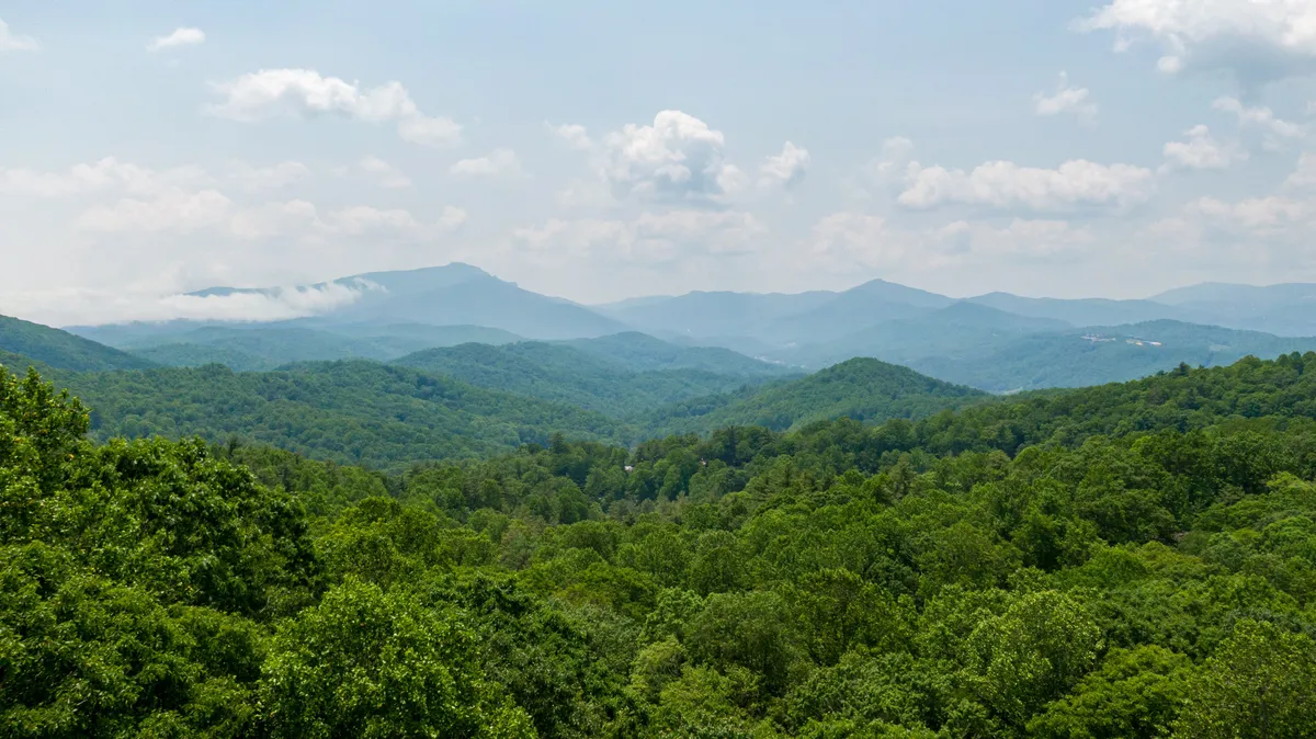A breathtaking view of distant Blue Ridge Mountains framed by lush green trees under a dramatic, cloudy sky. The scene evokes the grandeur and beauty of Western North Carolina’s outdoors, suggesting the proximity of nature and the promise of exploration.
