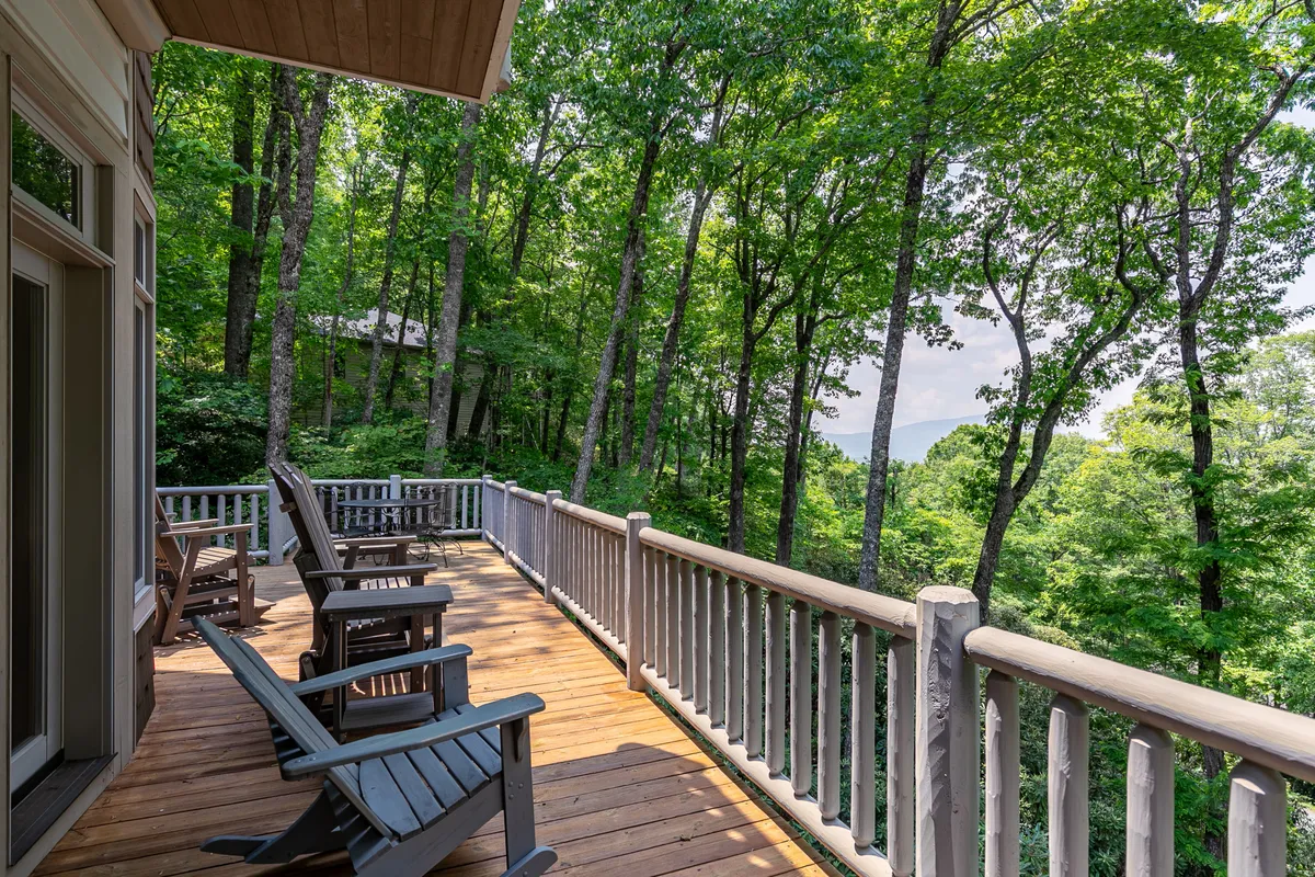 An exterior wooden deck nestled among tall trees, furnished with Adirondack chairs. The serene atmosphere invites relaxation, reading, and connection with nature amid lush greenery.