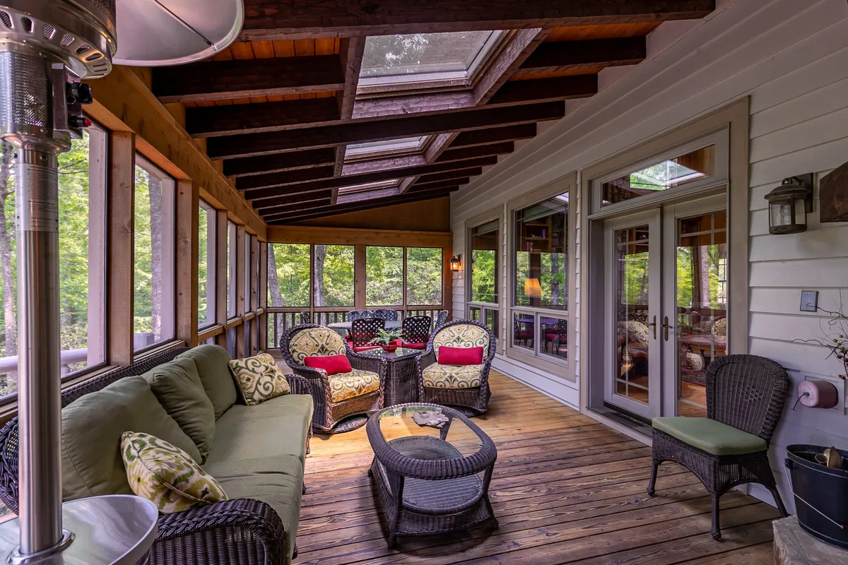A spacious, sunlit living area with comfortable seating positioned near large windows and skylights. Plush decorative cushions and a coffee table enhance the welcoming atmosphere, while the extensive windows provide captivating views of the outdoors in every season.