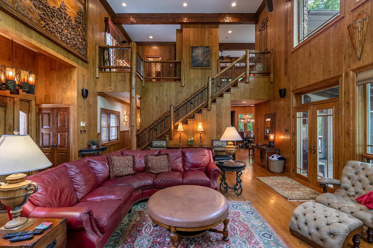 A spacious living area with a large leather sectional sofa and round coffee table, framed by a wooden staircase and expansive windows. The space exudes comfort and is designed for both casual relaxation and lively gatherings, enhanced by curated art on the walls.