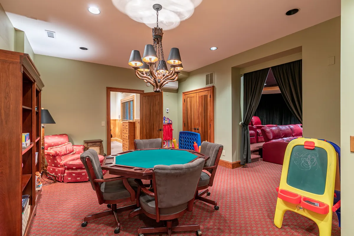 A dedicated poker area featuring a classic poker table, red armchairs, and a playful children's art corner with an easel. The space is illuminated by a chandelier, creating a cozy environment perfect for family tournaments and gatherings.