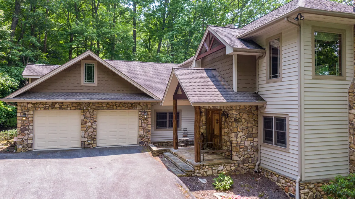 This image showcases the stone facade and wooden porch of Amitola, surrounded by lush greenery and the sloped roof typical of a mountain retreat. The home is set against a tranquil natural backdrop, inviting guests to connect with the outdoors from the very first glance.