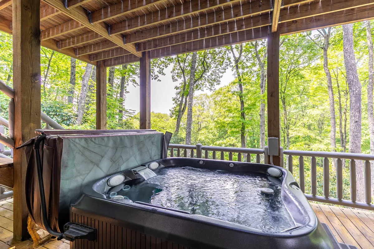 A secluded hot tub set on a wooden deck surrounded by trees and a rustic railing. The scene suggests quiet moments of relaxation, stargazing, or unwinding after a day of group activities in a tranquil, private setting.