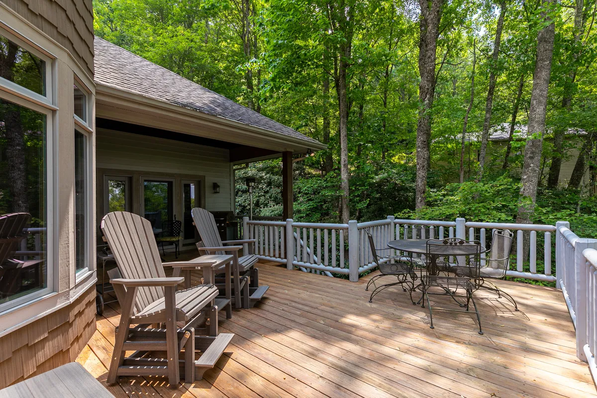 The wooden deck is outfitted with rocking chairs and an outdoor dining table, surrounded by mature trees. The tranquil outdoor space offers a peaceful spot to relax, dine, or share stories after a day of sightseeing and adventure.