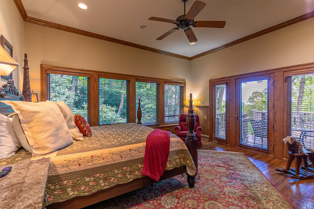 A tranquil bedroom featuring a comfortable bed, large windows that welcome natural light, a rocking chair, and decorative pillows. The view outside blends seamlessly with the room, creating a peaceful retreat.