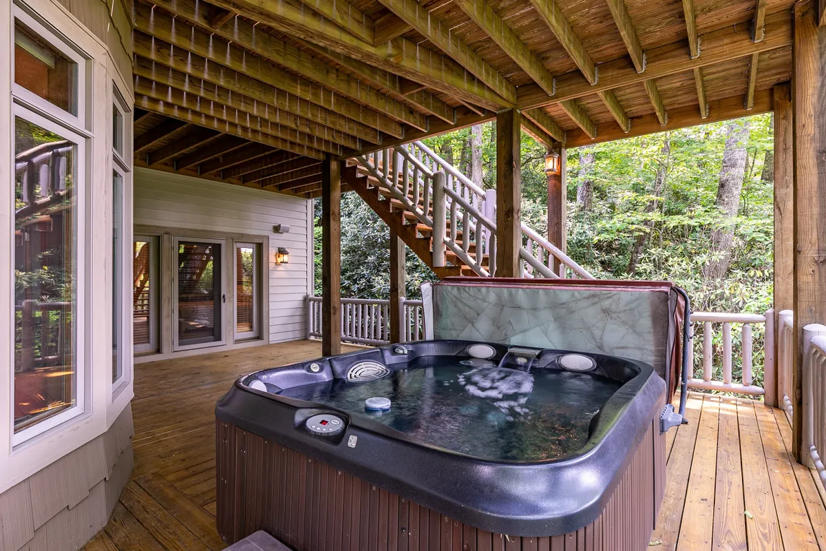 The exterior deck features a bubbling hot tub with wooden deck flooring and steps leading up. The hot tub overlooks natural greenery, providing a private spot for relaxation under the stars or after a day of mountain activity.